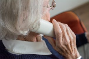 older woman with gray hair holding a white phone up to her ear. 