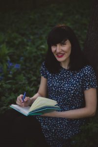 caucasian woman sitting outside writing in a journal while smiling
