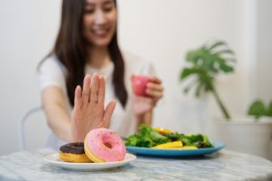 caucasian woman sitting down pushing donuts away and has a salad in front of her.
