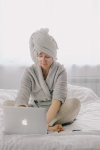 older caucasian woman sitting in a robe with a towel on her head looking at her laptop