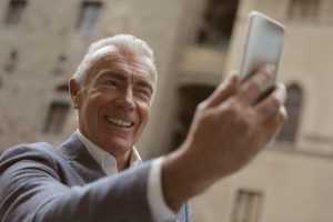 older caucsasian man holding a cell phone up smiling