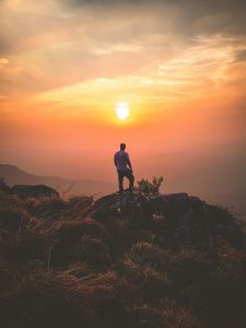 man standing at a cliff while the sun sets