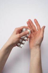 persons hands with their thumb popping out a white pill from a pill pack.