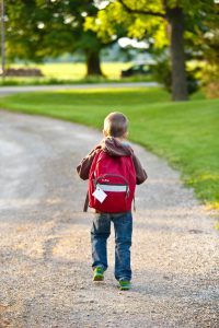 the back of a kid walking down a road with a backpack on.