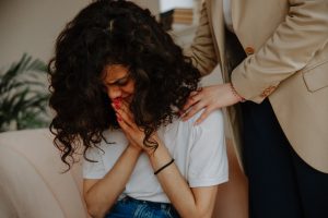woman with her head down and another womans hands on her shoulders