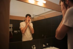 man standing in the mirror holding his cheeks with both hands