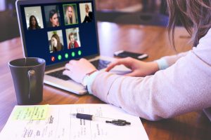 persons hand on a laptop keyboard with zoom screen of people