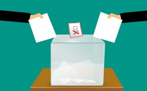 people's hands putting a sheet of paper in a ballot box