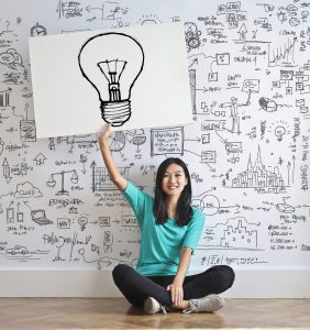 woman sitting down with a light bulb drawn on a paper holding it over her head.