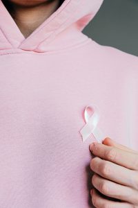 caucasian person wearing a pink hoddie while holdikng a pink ribbon up to their chest area