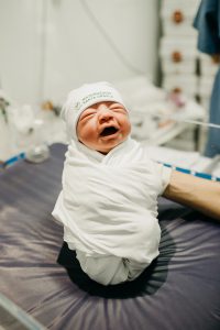 newborn baby in a white cap and swaddle