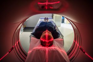 caucasian person sitting in an MRU machine with the red lasers cross pointed on their head.