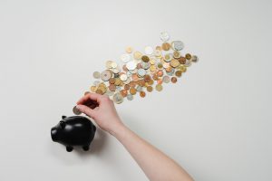 caucasian hand putting coins into a black piggy bank. 