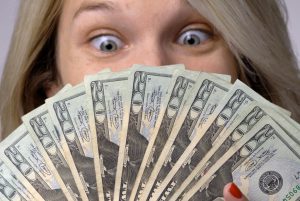 caucasian woman's eyes staring at twenty dollar bills in her hand.