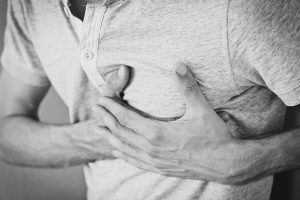 black and white picture of a mans torso with his hands holding his heart area.