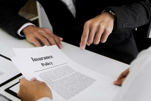body in a suit with caucasian hands pointing at an insurance policy that is being held by another set of hands