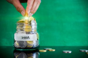 caucasian hand putting a coin into a clear jar labeled hsa on it