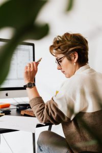 caucasian woman looking at papers on a table while in front of a laptop