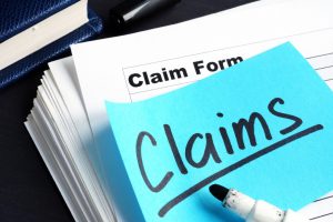claims written on a blue post it note that is on top of a stack of paperwork with the word "claim form" on the top