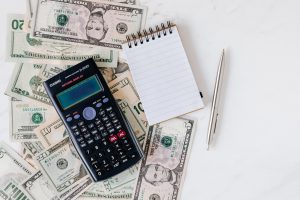 calculator laying on top of money bills and a notepad next to it