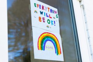 everything will be okay written on a poster with a rainbow on the bottom that is taped to a window