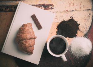 cup of black coffee with a croissant and piece of chocolate on a plate next to the cup