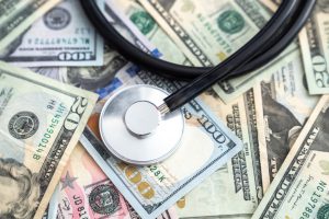 money bills spread out on a table with a stethoscope on top of it.