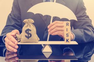 person holding an umbrella with a seesaw with a bag of money on one end and the word risk on the other end.