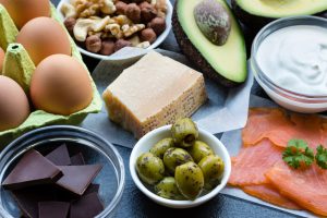 eggs, olives, salmon, avocado, cheese, and dark chocolate on a table