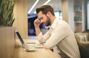 caucasian man looking down at his laptop with his hand to his forehead