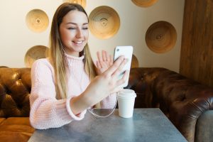 caucasian woman holding her white phone up smiling and waving at the screen.