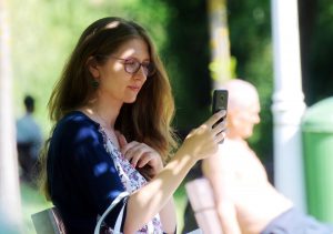 caucasian woman sitting outside with her phone up to her face looking at it with a smile