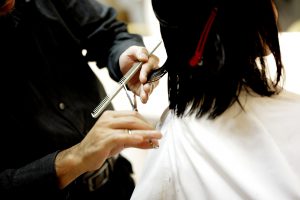back of a woman's head getting her hair cut by a pair of hands.