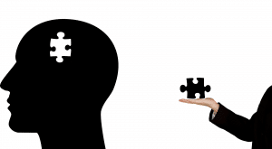 black silhouette of a head with a white puzzle piece and a persons hand holding the black missing puzzle piece.