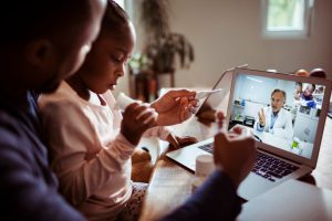 young african american girl holding a thermometer in her hand with a doctor on the laptop screen.