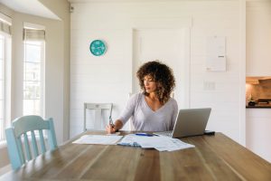 woman with curly hair sitting at her table with laptop open and a calculator in front of her and a pen in her hand.