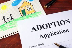 adoption application with another paper with a drawing of a house and parents holding a kids hand