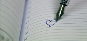 opened notebook with a pen writing a little heart in the middle of the page.
