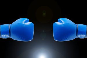 two blue gloves facing each other with a black background and a light shining on the bottom middle of the picture.