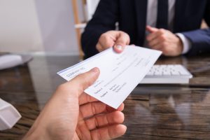 person sitting on a chair with a suit on handing another hand a check