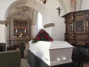 white casket in a church with red roses placed over it