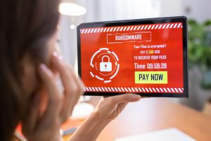 a woman holding up a tablet with a red screen and the word ransomware on it