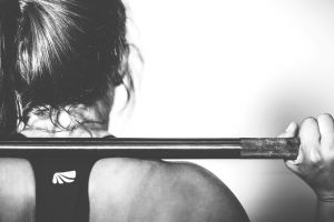 black and white picture of the back of a woman with a weight bar on her shoulder