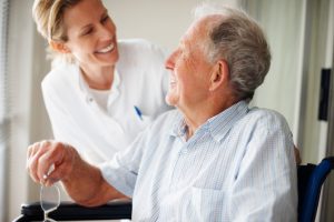 older caucasian man with a button up on and a caucasian woman with lab coat checking on him.