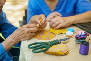 older hands holding a piece of construction paper with a person in blue scrubs sitting next to them
