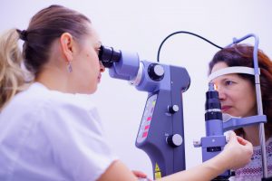 caucasian woman looking into eye machine to look at an other womans eye that has a laser light on it