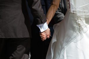 two hands holding each other, one of a man in a suit and the other a woman's in a wedding gown