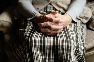 caucasian hands holding each other on a woman's lap with a skirt and cardigan on