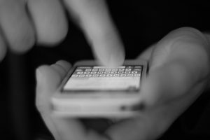 black and white picture of a hand holding a cell phone with the other handing texting with a finger