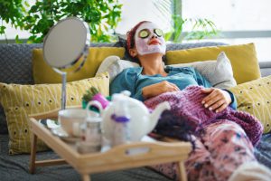 woman laying on her couch with a face mask and tea on a table.